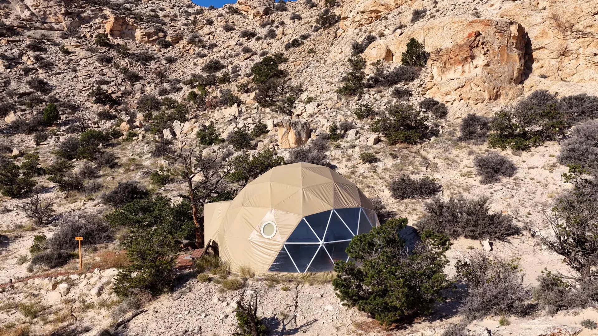 Aerial view of the geodesic dome at Luxe Den Capitol Reef, its window wall facing out among junipers below white sandstone cliffs near Torrey, Utah