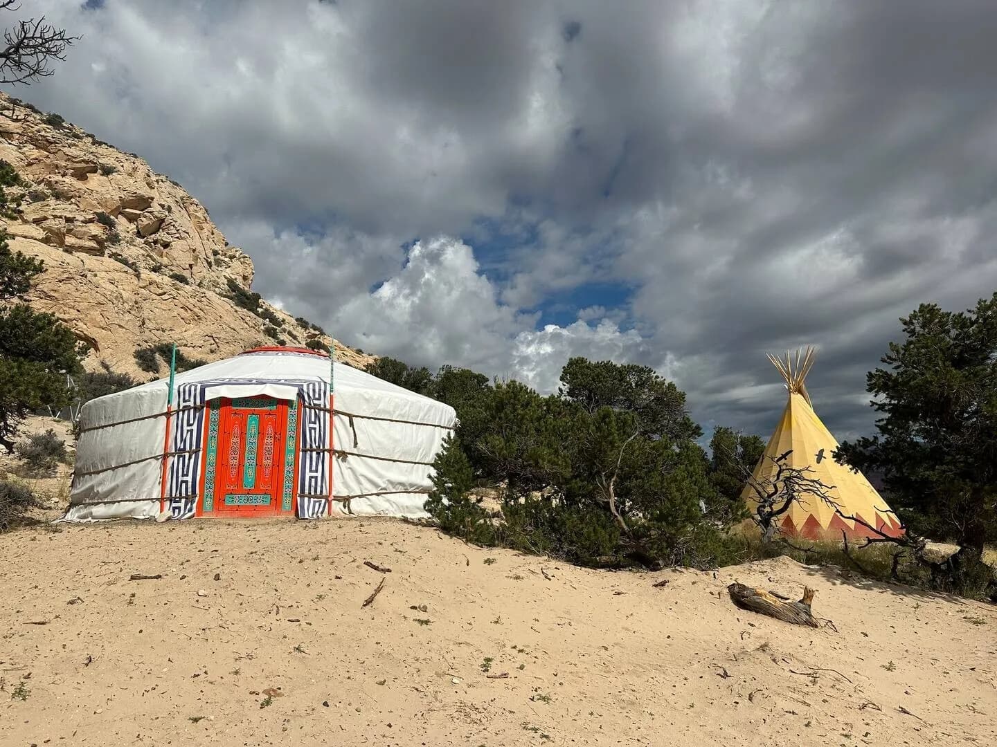 The Hilltop Mongolian yurt with a tipi behind it, under a stormy sky
