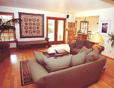 The inn's living room around 2003: sofas around a coffee table, a quilt on the wall, wood floors and french doors