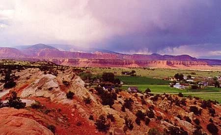 A storm over the red cliffs above Teasdale, Utah, with the green valley floor and the town below