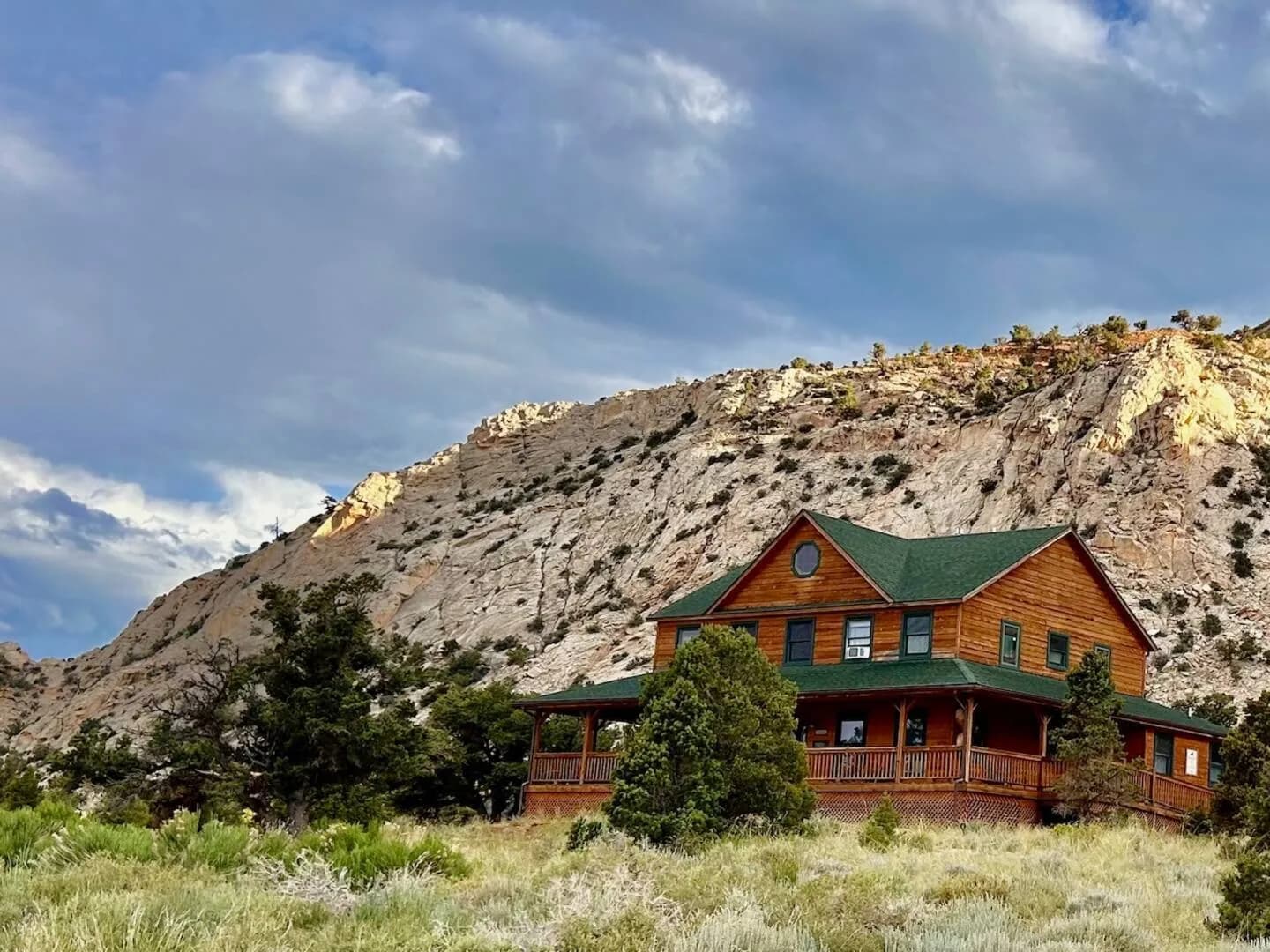 The Lodge, a two-storey timber building with a green roof and a wraparound deck, below a white sandstone ridge