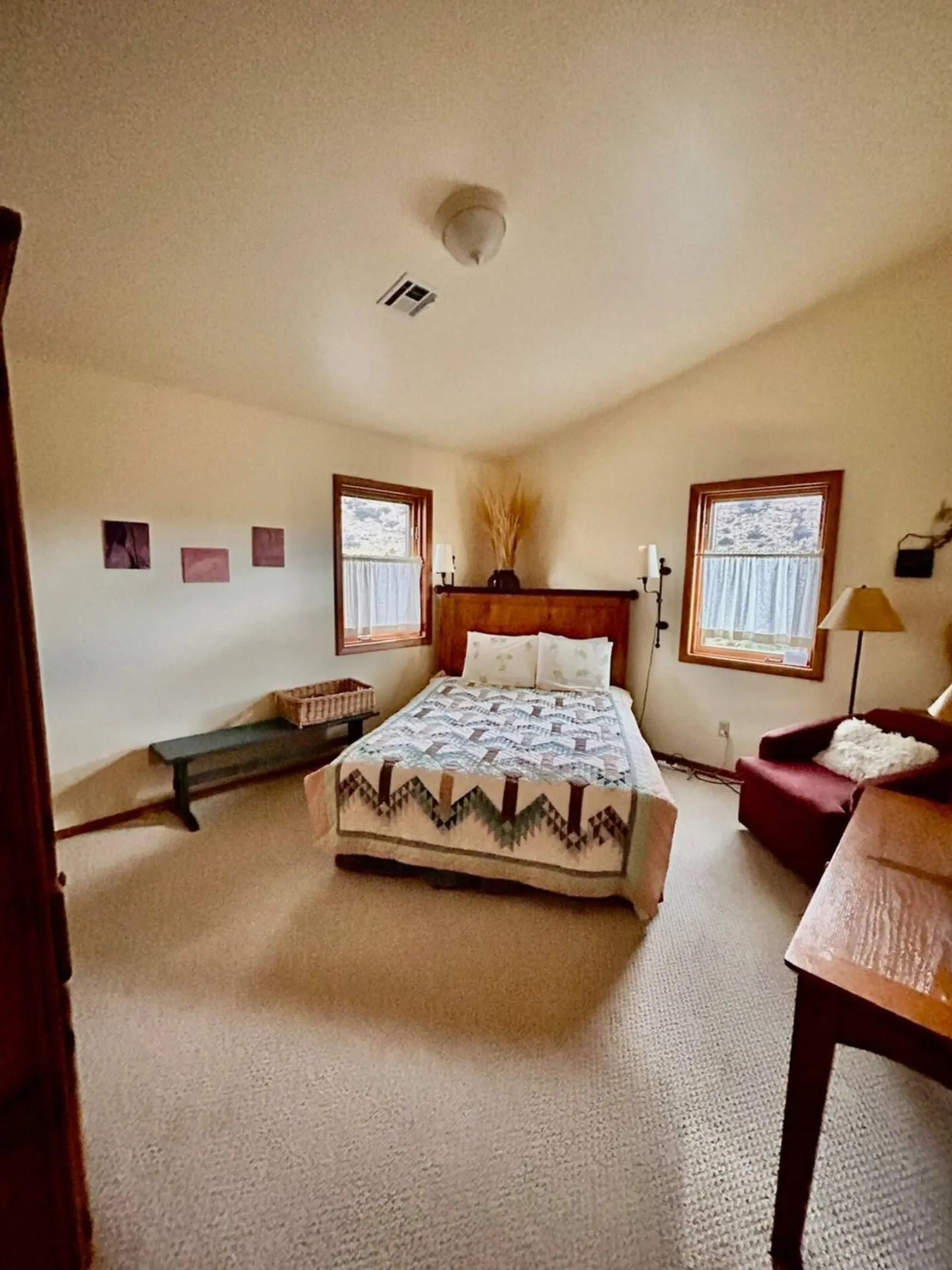 A bedroom in The Lodge with a vaulted ceiling, a bed under framed pictures and a corner table