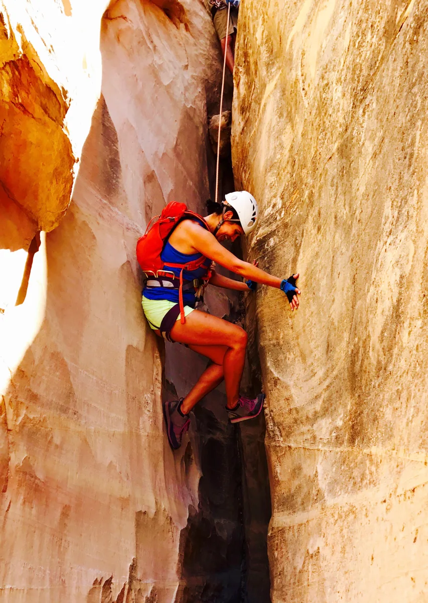 A canyoneer in a helmet stemming up a narrow sandstone slot