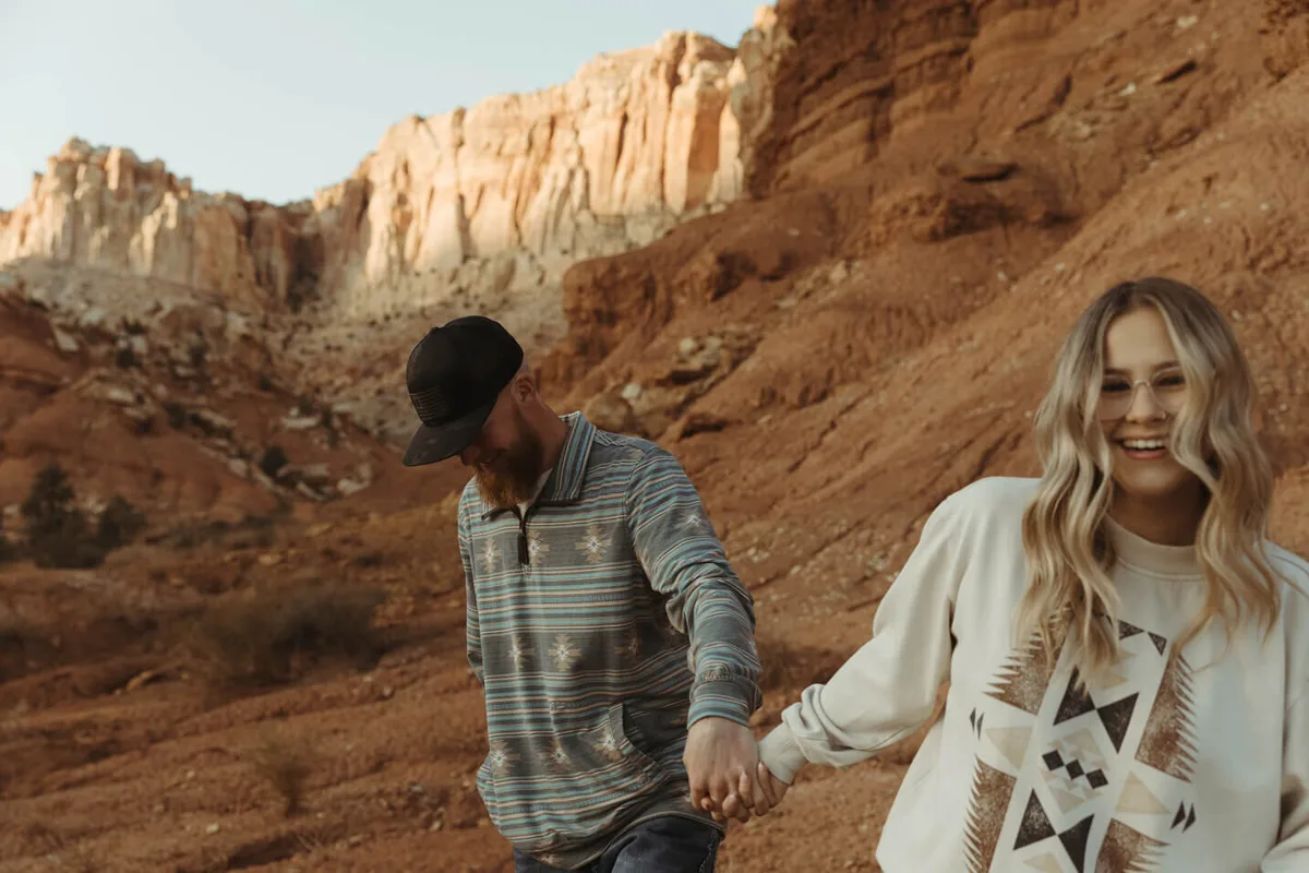A laughing couple walking hand in hand through red rock